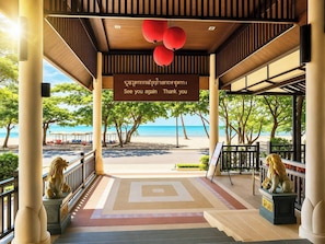 A covered outdoor area with a view of the beach, a sign with a message, and lion statues. - Royal Heritage Pavillion (Pattaya)