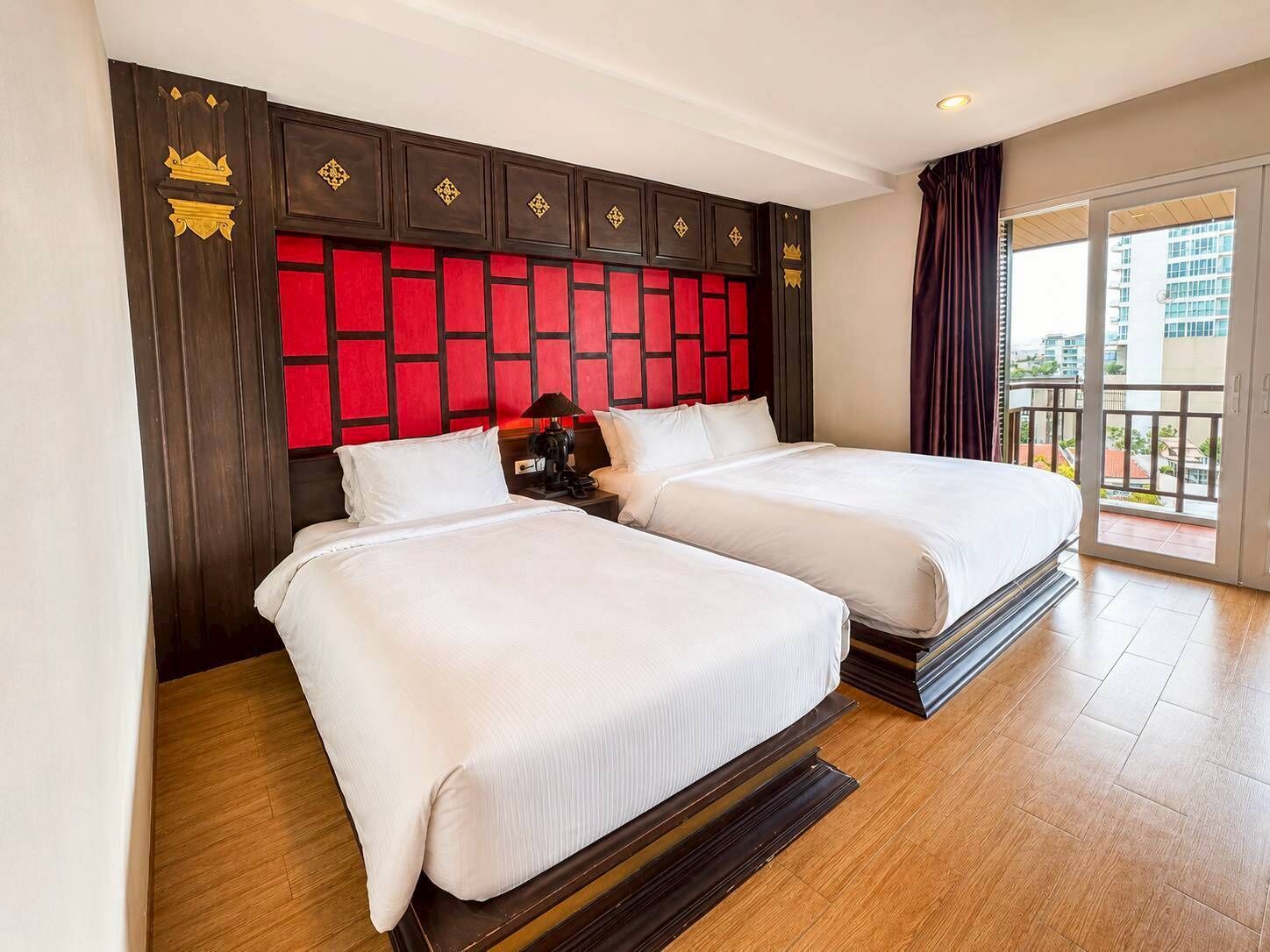 A hotel room with two beds, a red and black headboard, and a balcony with a city view.