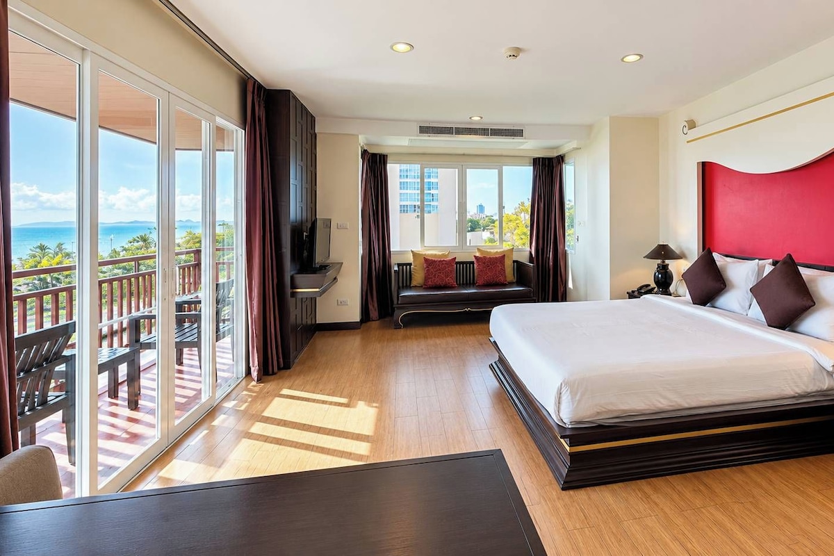 Habitación de hotel con una cama grande, un escritorio, una silla y un balcón con vista al océano.