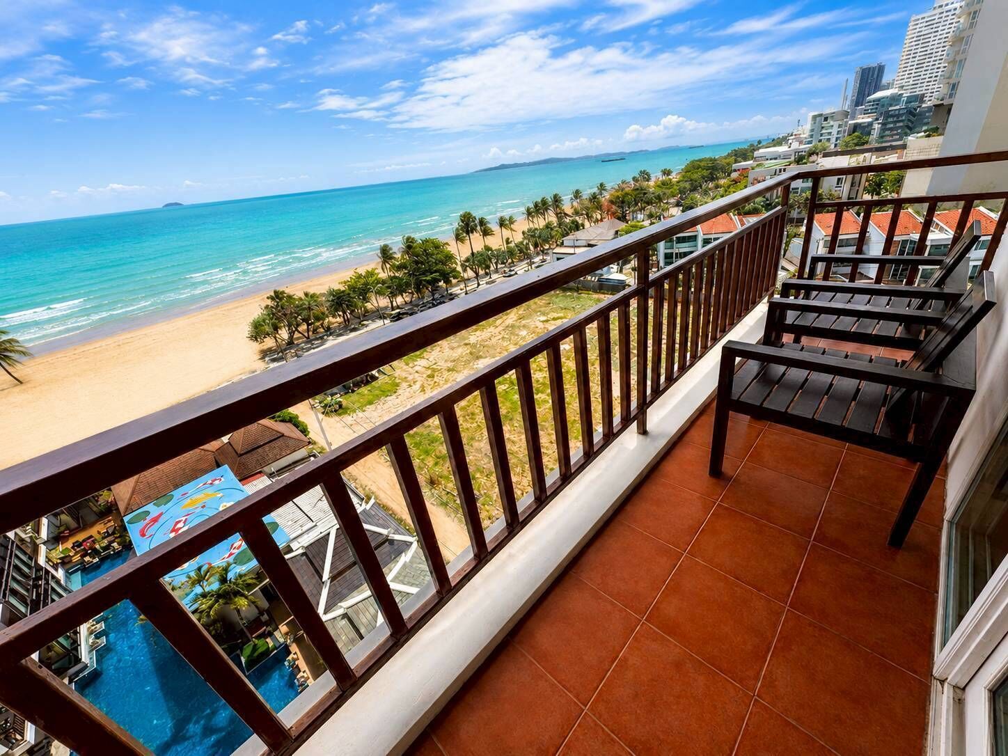 Uma varanda com vista para uma praia e oceano, piscina e edifícios modernos ao fundo.
