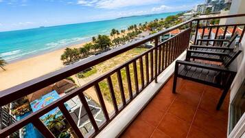 Uma varanda com vista para uma praia e oceano, piscina e edifícios modernos ao fundo.