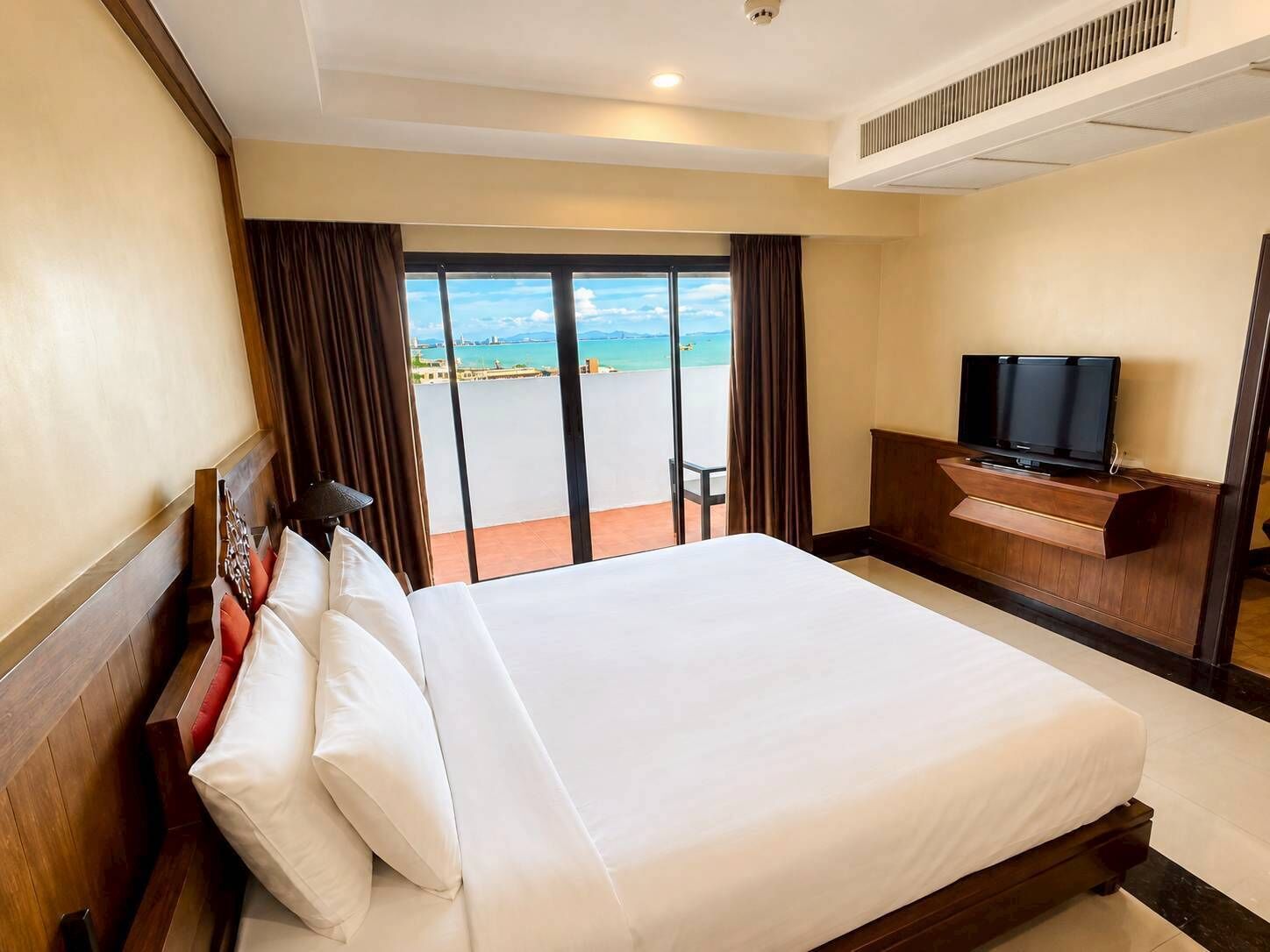 A hotel room with a large bed, a TV, and a view of the sea.