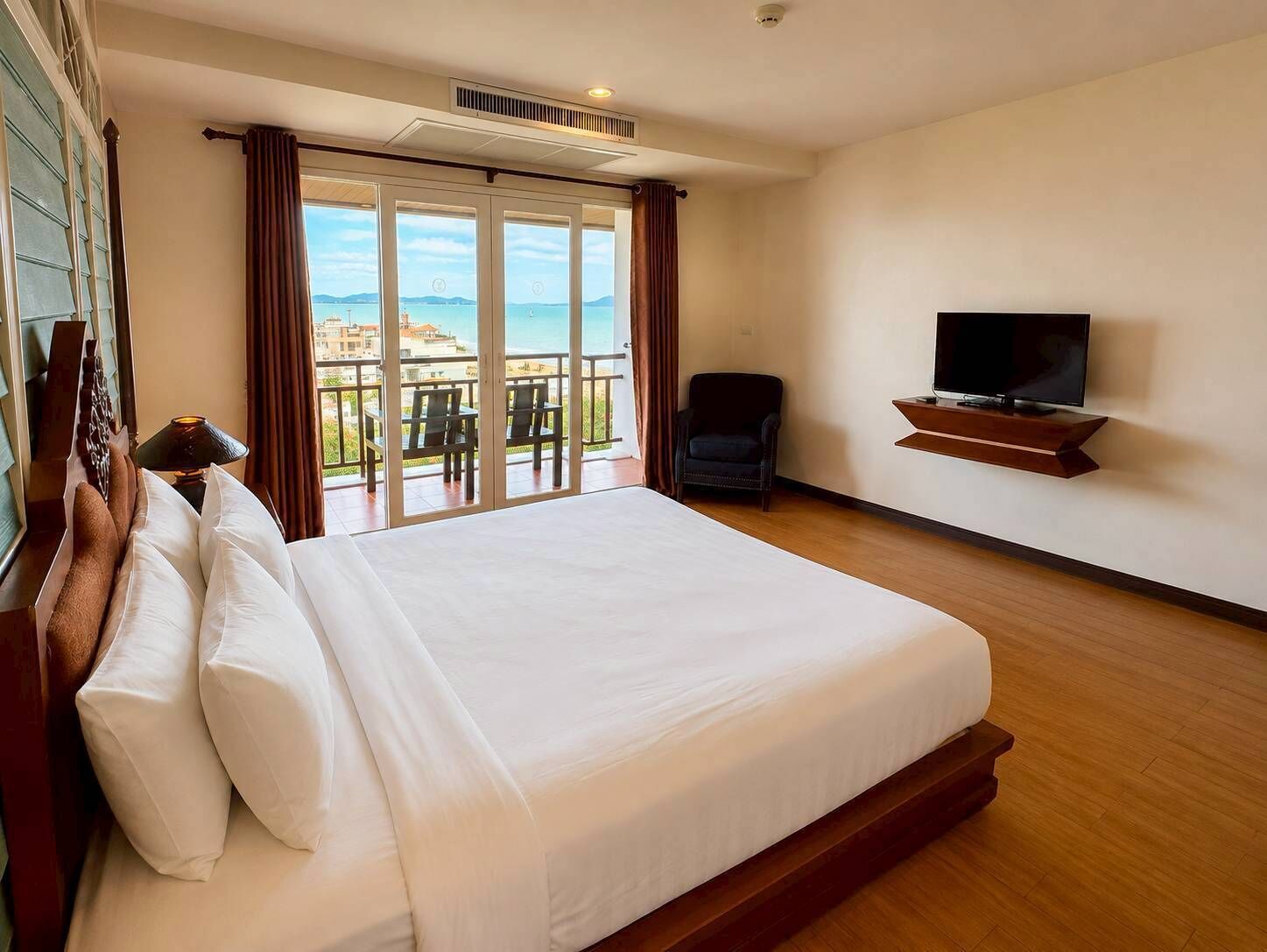 A hotel room with a large bed, a TV, a chair, and a balcony with a view.