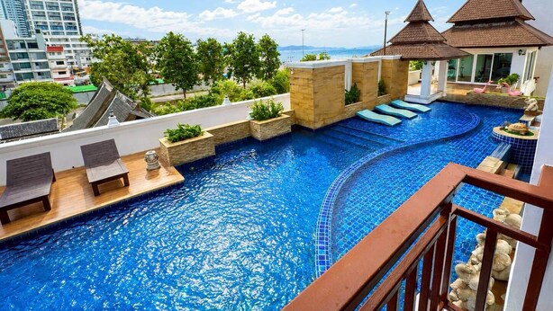 A rooftop infinity pool with a view of the ocean, surrounded by lounge chairs and potted plants.