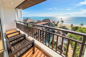 A balcony with a wooden floor and metal railing overlooking a beach and ocean.