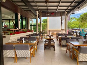 Een restaurant met terras, inclusief tafels en stoelen, onder een overdekt gebied met uitzicht op de omgeving.