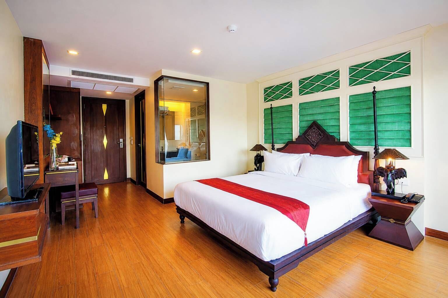 Habitación de hotel con una cama grande, un escritorio, una silla, un televisor y una ventana con persianas verdes.