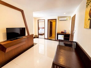 Een hotel lobby met een houten receptiebalie, een flatscreen televisie, een eethoek met een bank en een gang naar een slaapkamer.