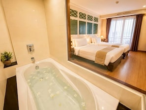 Une chambre d’hôtel dotée d’une grande baignoire, d’un lit avec de nombreux oreillers et d’un grand miroir qui reflète la pièce.