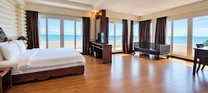 A hotel room with a large bed, a TV, a desk, and a balcony with a view of the sea.
