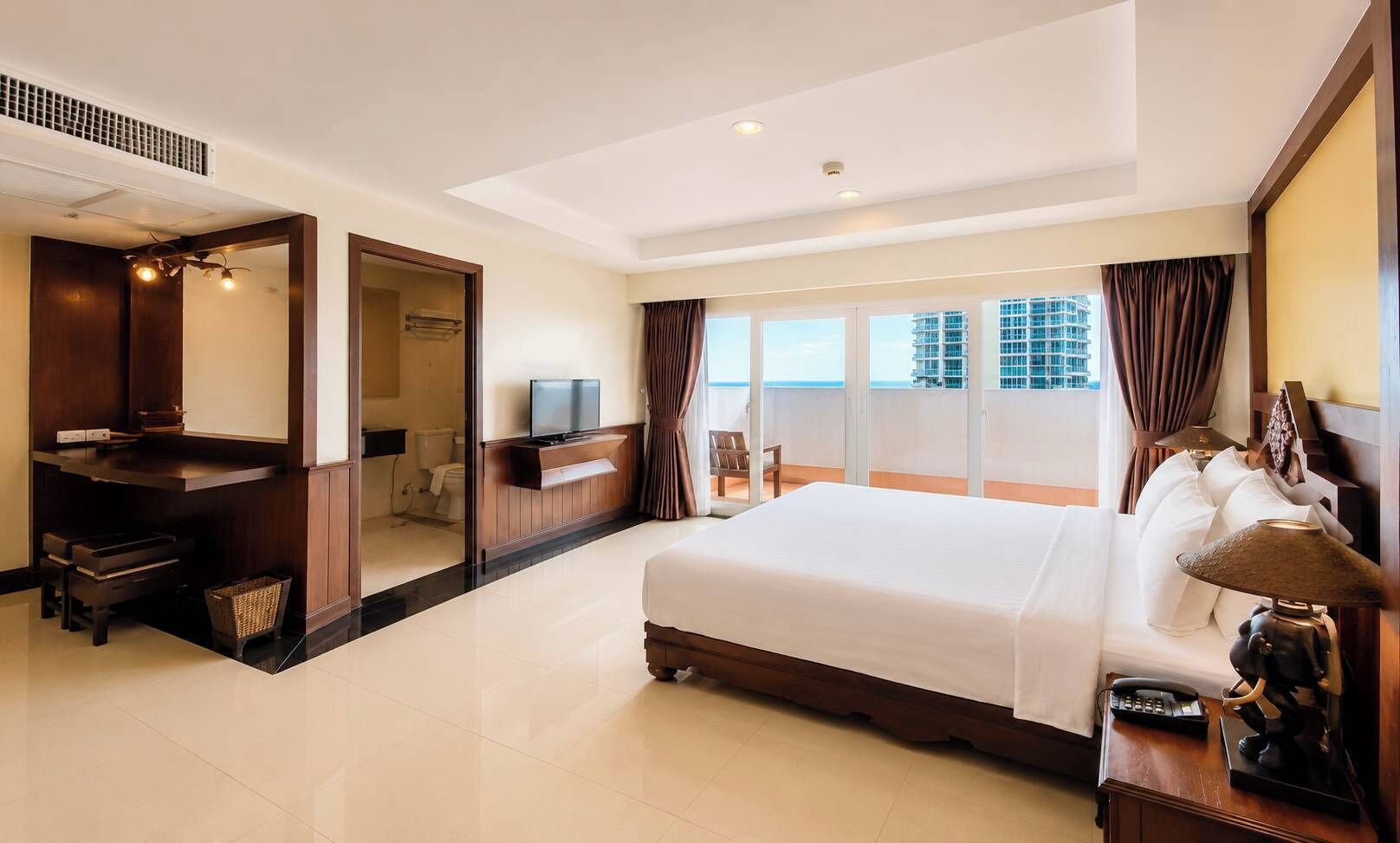 Ein Hotelzimmer mit einem großen Bett, einem Schreibtisch mit Fernseher, einem Balkon mit Blick auf Gebäude und einem Badezimmer mit Dusche und Toilette.