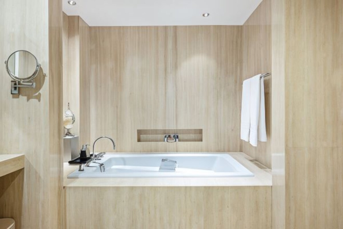 A modern bathroom with a large bathtub, a wall-mounted mirror, and a towel rack.
