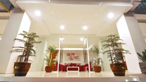 A lobby with a reception desk, potted plants, and a red sofa. - Tickle Hotel (Yogyakarta)