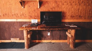 A wooden desk with a television, a small shelf above it, and a sign on the wall. - Mountain View Cabins (Golden)