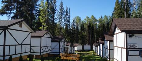 A row of traditional timber-framed cottages with a sign indicating accommodations available from 1-8 and 9-15.