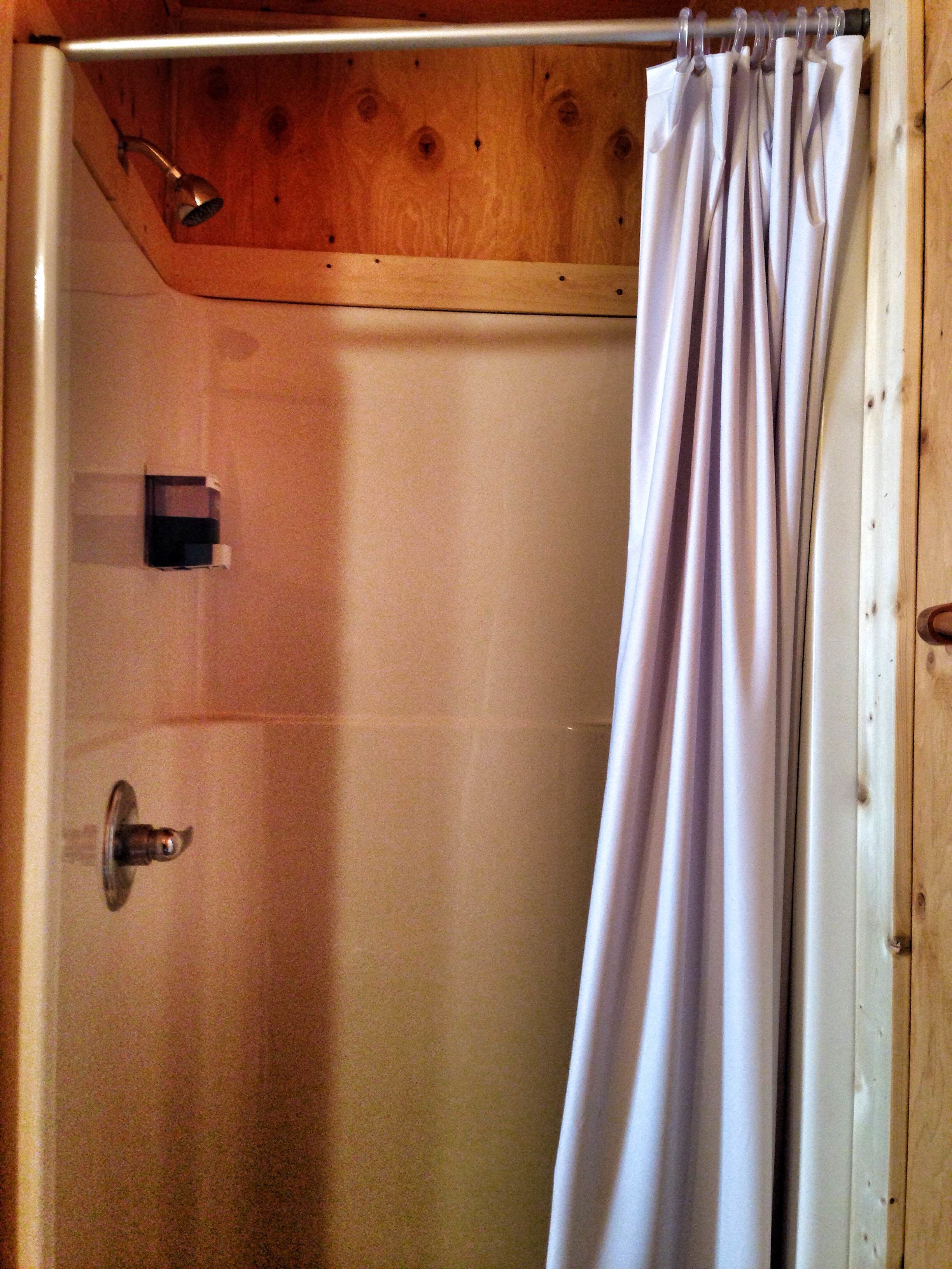 A shower with a wooden door and a white curtain.