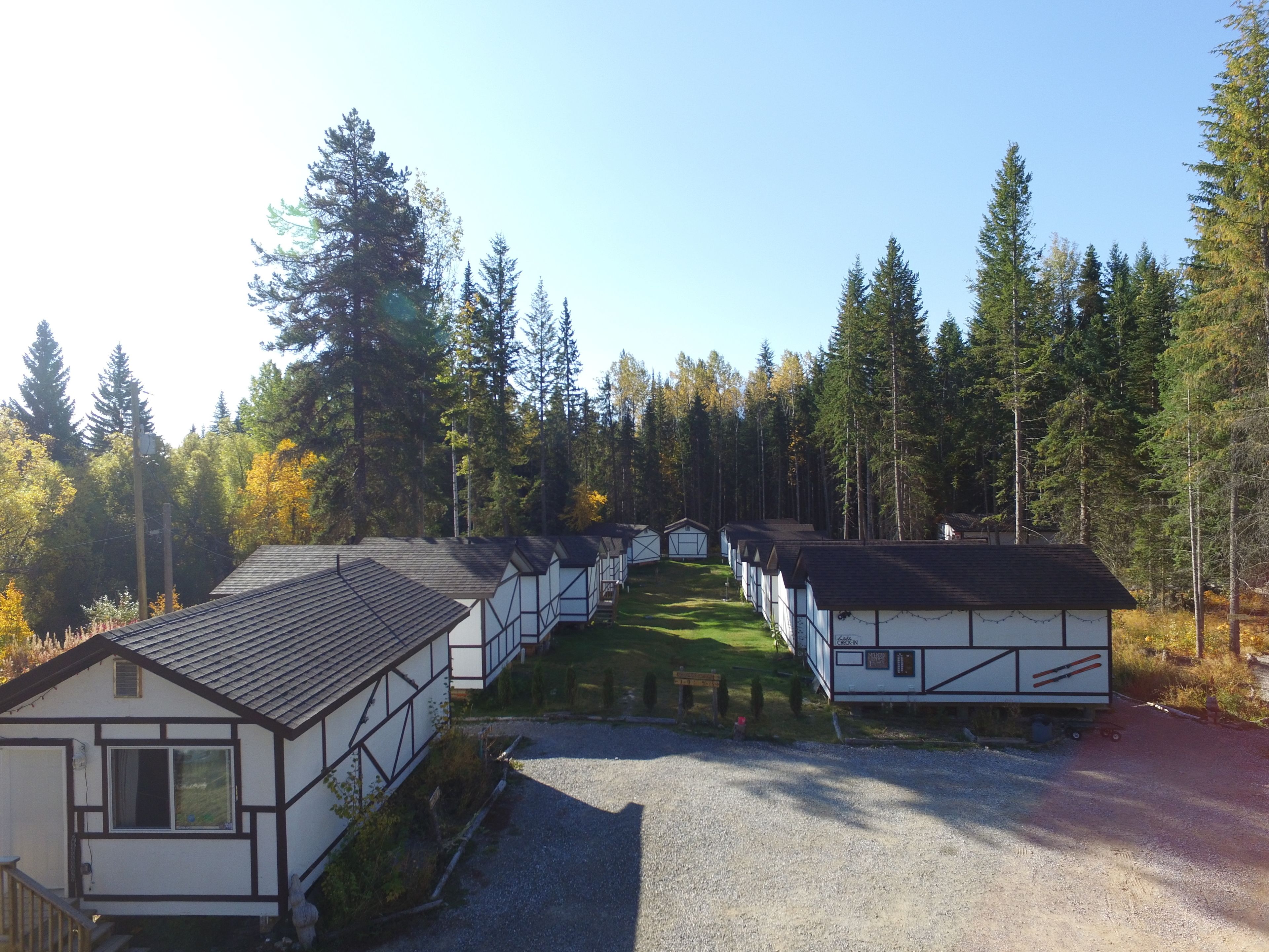 A row of traditional timber-framed cabins with a gravel driveway and a forested backdrop.