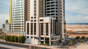 Et moderne hotel med et tydeligt 'S'-logo, en buet glasfacade og udsigt til stranden.