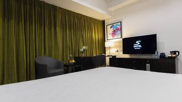 Una habitación de hotel con una cama grande, televisión, escritorio con silla y cortina verde.