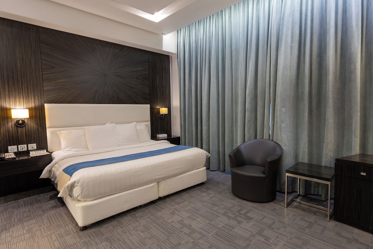 A hotel room with a large bed, a desk, a chair, and a wardrobe.