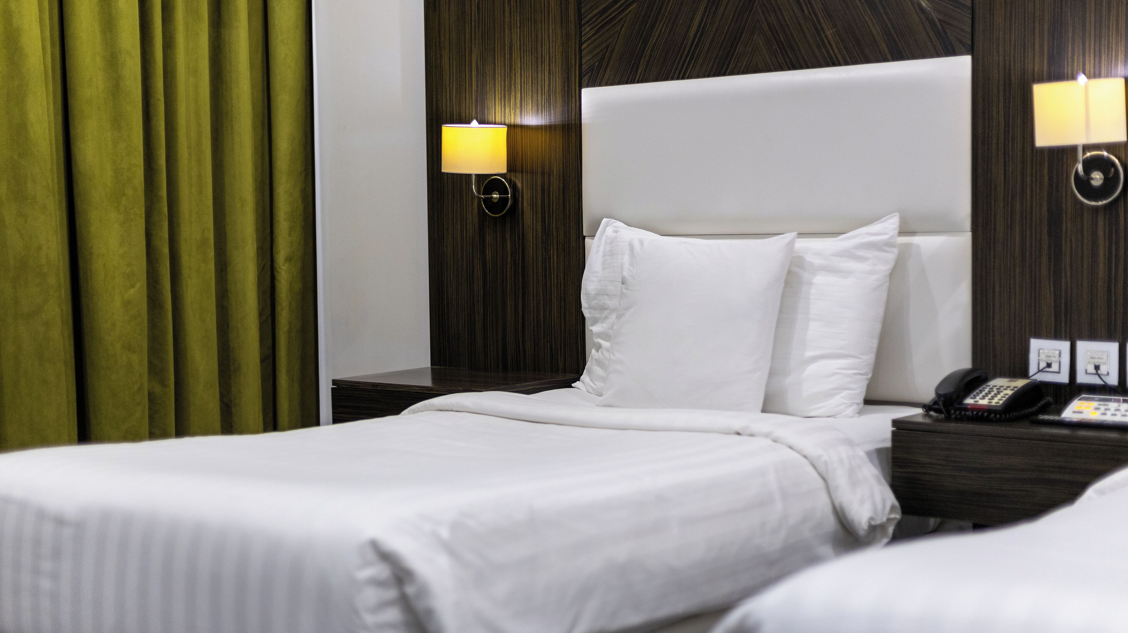 A hotel room with a large bed, two bedside tables, a telephone, and a wall-mounted lamp.