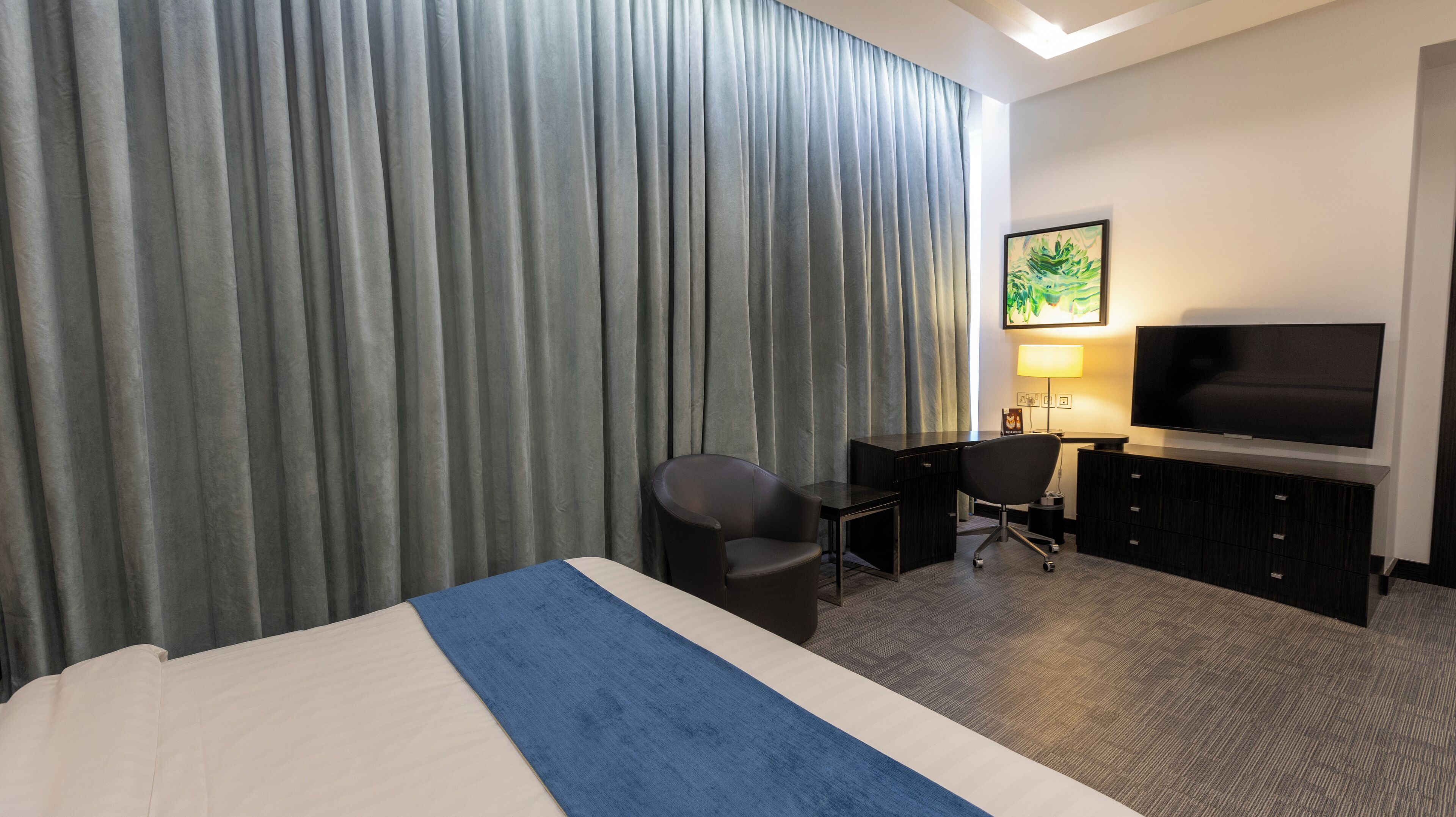 A hotel room with a bed, a desk, a chair, a television, and a large window with curtains.