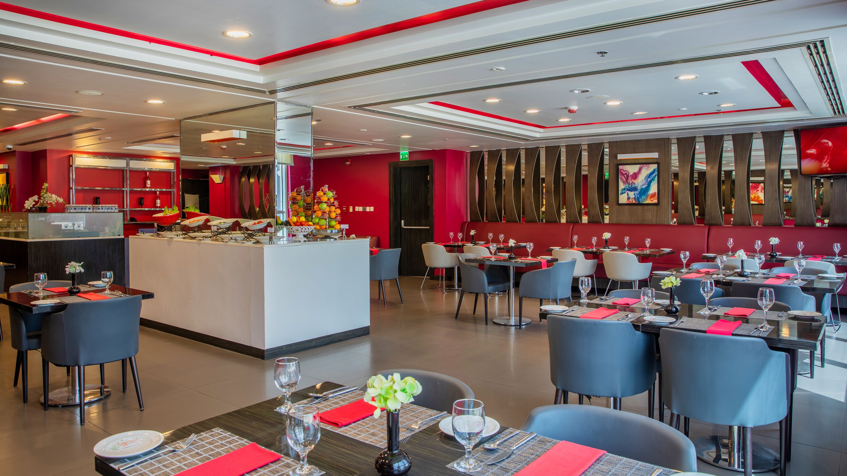 Un restaurante moderno con una barra central, varias mesas para comer con sillas y una decoración en tonos rojo y blanco.