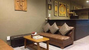 A reception area with a brown leather sofa, patterned cushions, a wooden table with a book, and a Buddha head sculpture on the wall. - Naturbliss Boutique Residence (Bangkok)