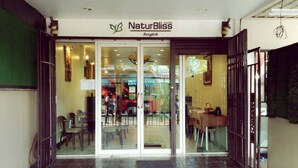 A restaurant entrance with a glass door, indoor seating visible through the door, and a sign reading "Nature Bliss Bangkok". - Naturbliss Boutique Residence (Bangkok)
