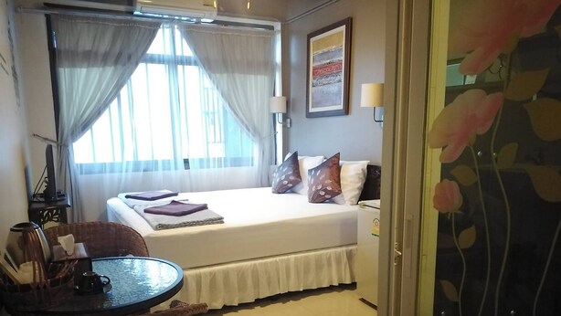 A hotel room with a bed, a small table, a chair, and a window with curtains. - Naturbliss Boutique Residence (Bangkok)