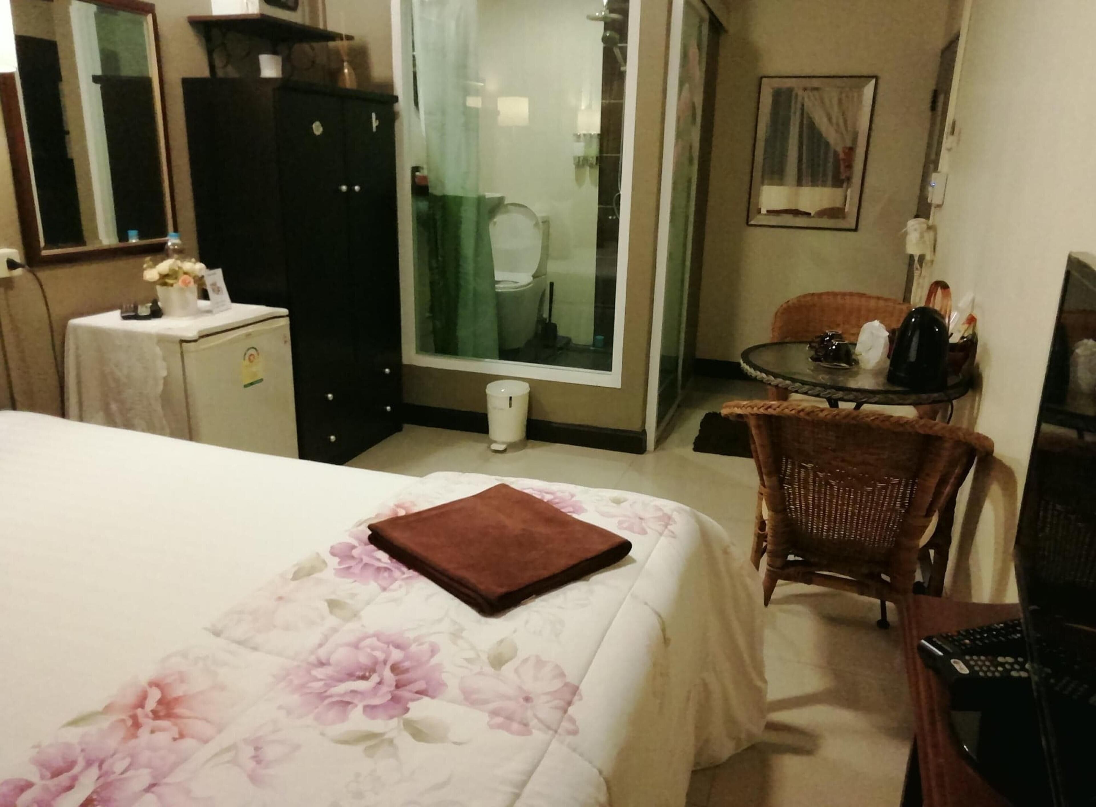 A hotel room with a bed, a desk, a chair, a wardrobe, and a bathroom visible through a glass door.