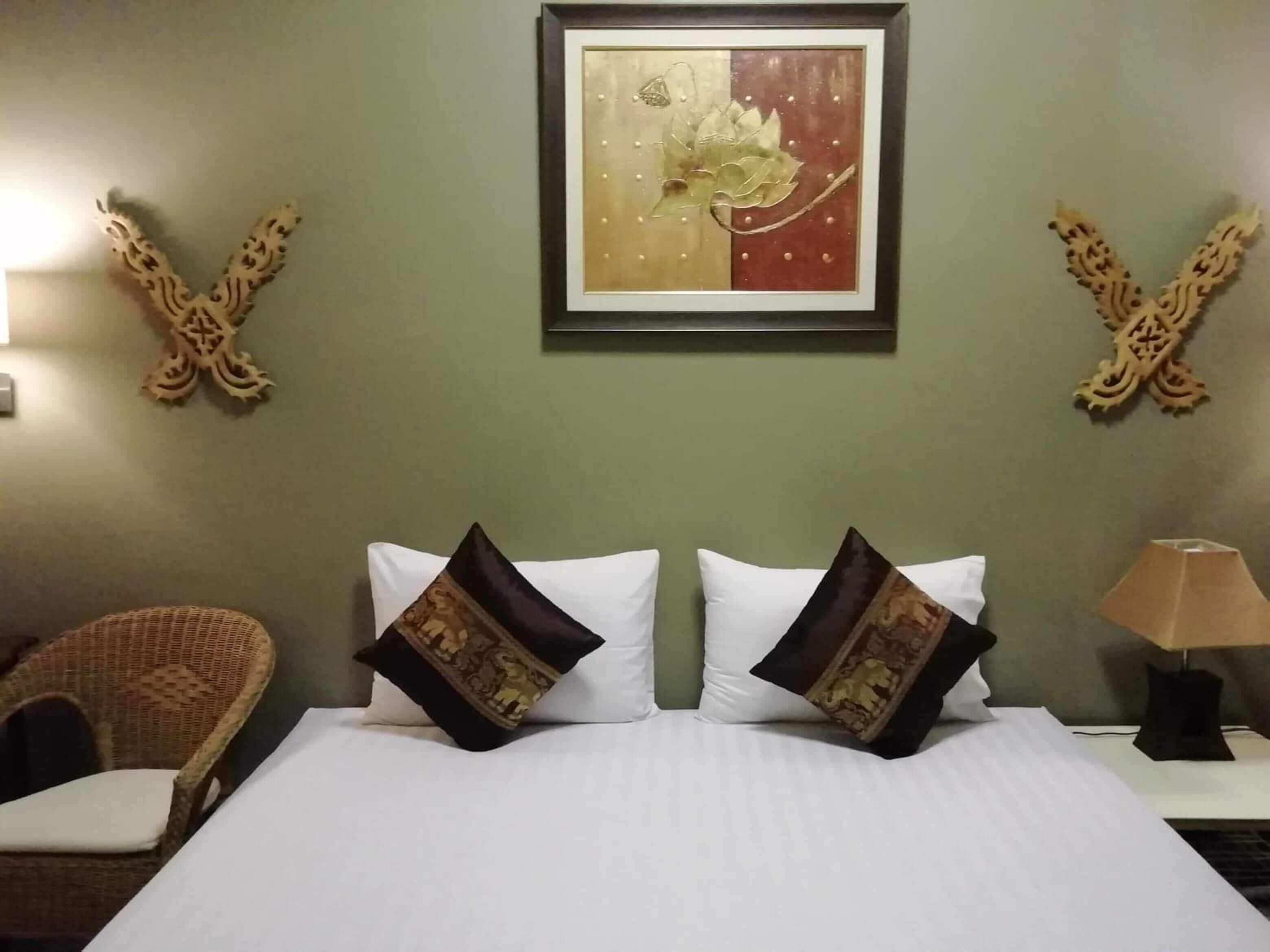 A hotel room with a bed, two pillows, a chair, a lamp, and a wall-mounted artwork.