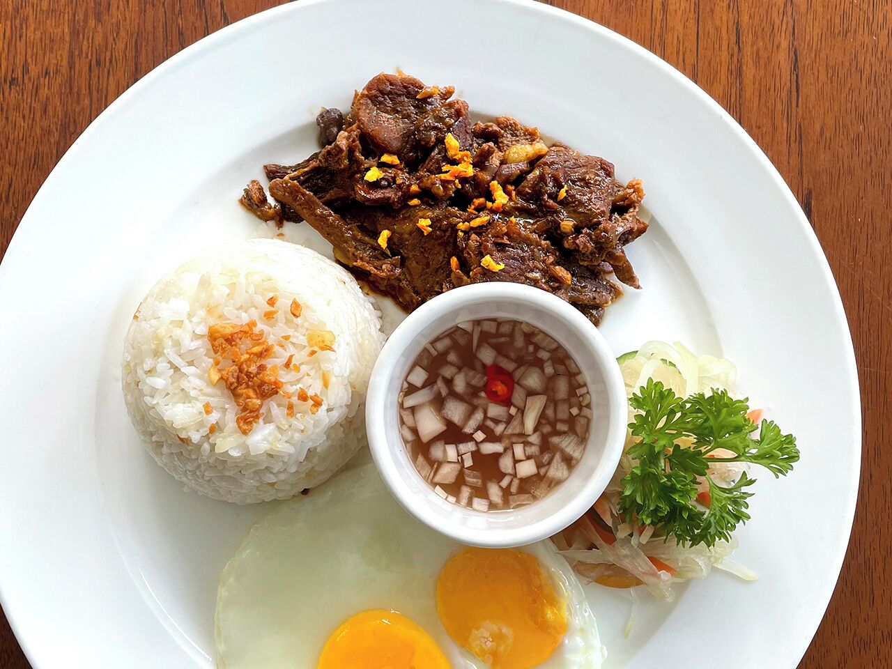 A plate with white rice topped with fried shallots, a bowl of clear soup with diced ingredients, and a side of fried egg.