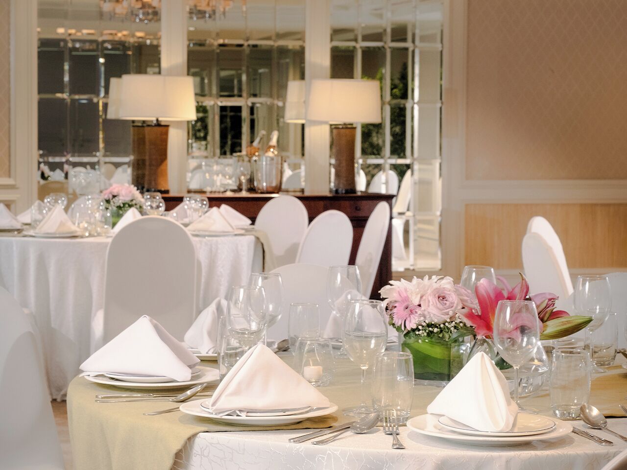 Un salón de banquetes con mesas redondas dispuestas para un evento formal, con manteles blancos, cristalería y centros de mesa florales.