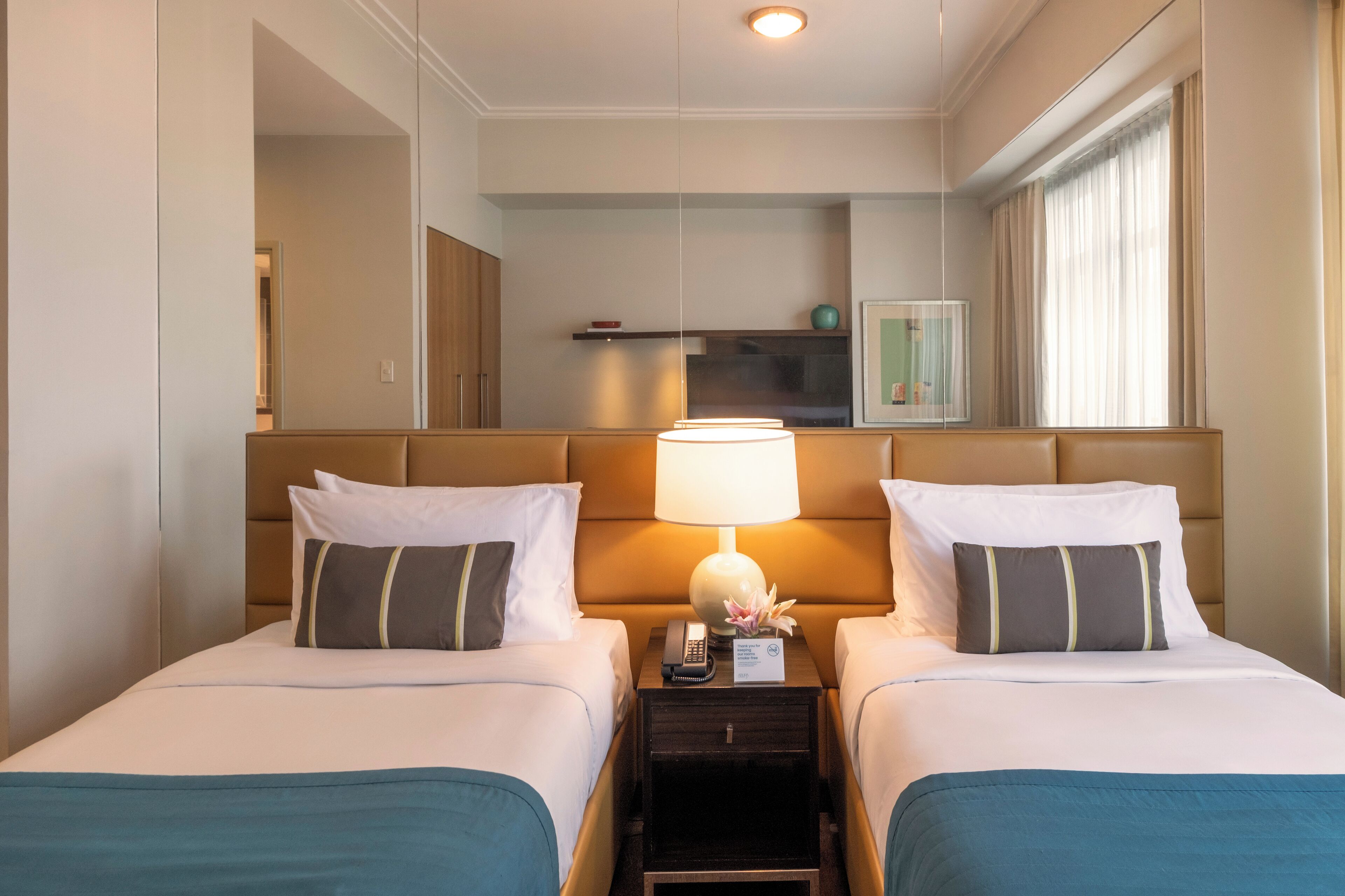 Een hotelkamer met twee bedden, een nachtkastje met een lamp, een telefoon en een tafeltje met een vaas.