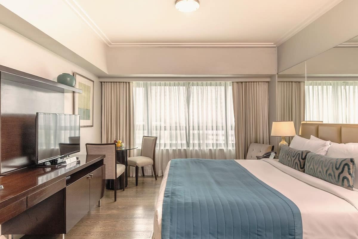 Habitación de hotel con cama, escritorio con televisor, silla y mesita de noche con lámparas.