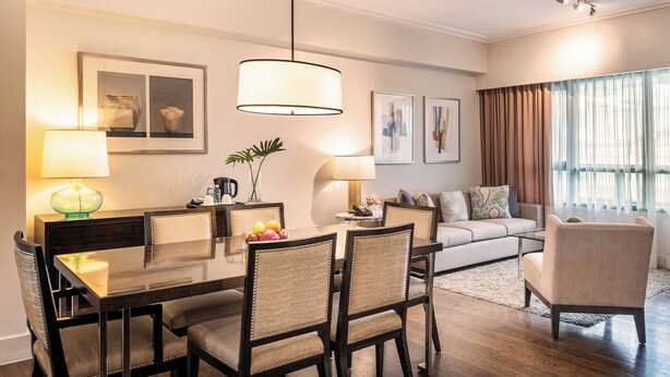 Un salon moderne avec un coin repas, comprenant une table à manger en bois, des chaises, un canapé et une table basse. On y trouve deux lampes fixées au mur, une plante en pot et des œuvres d’art encadrées qui décorent les murs.