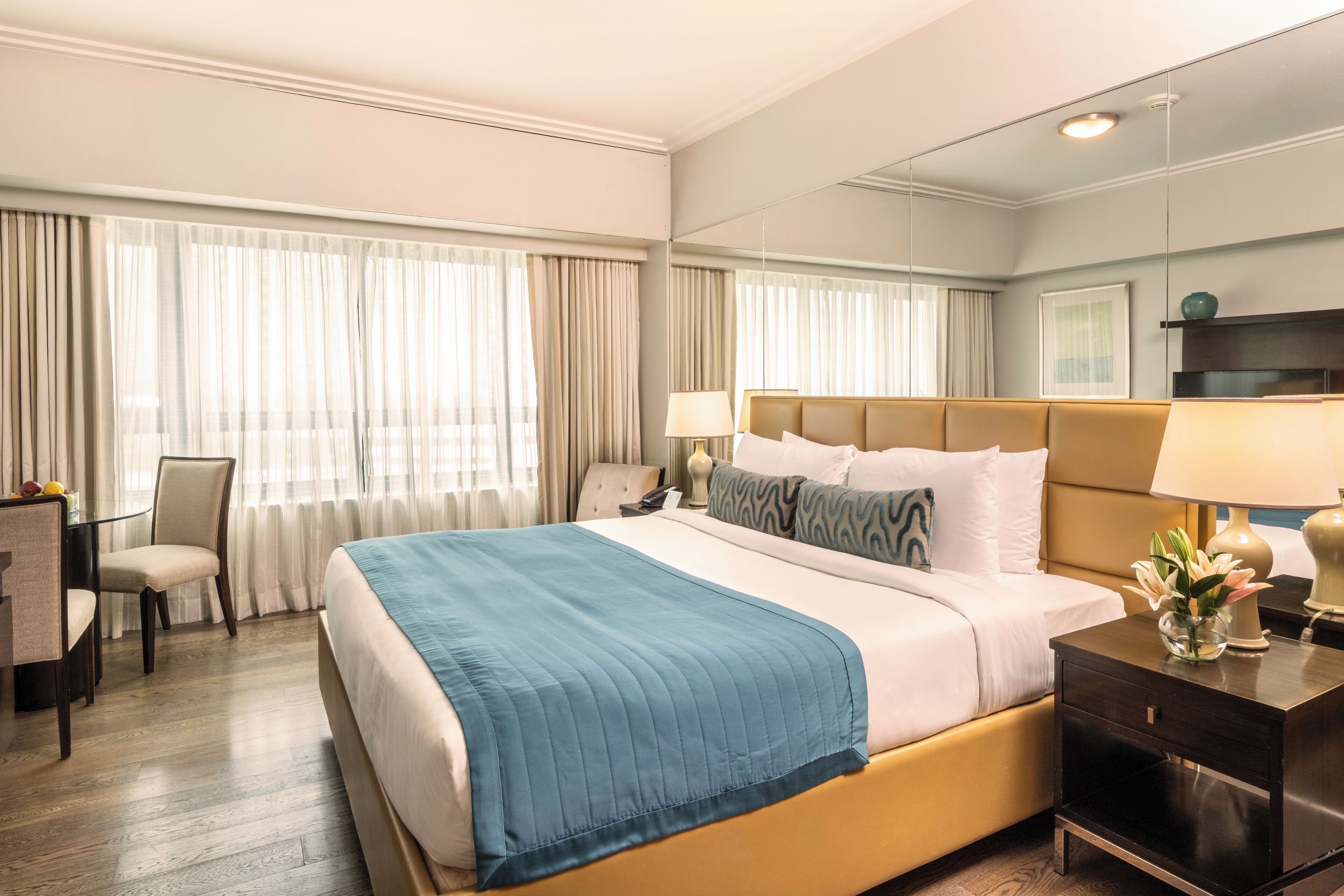 A hotel room with a large bed, a desk, a chair, and a nightstand with a lamp.