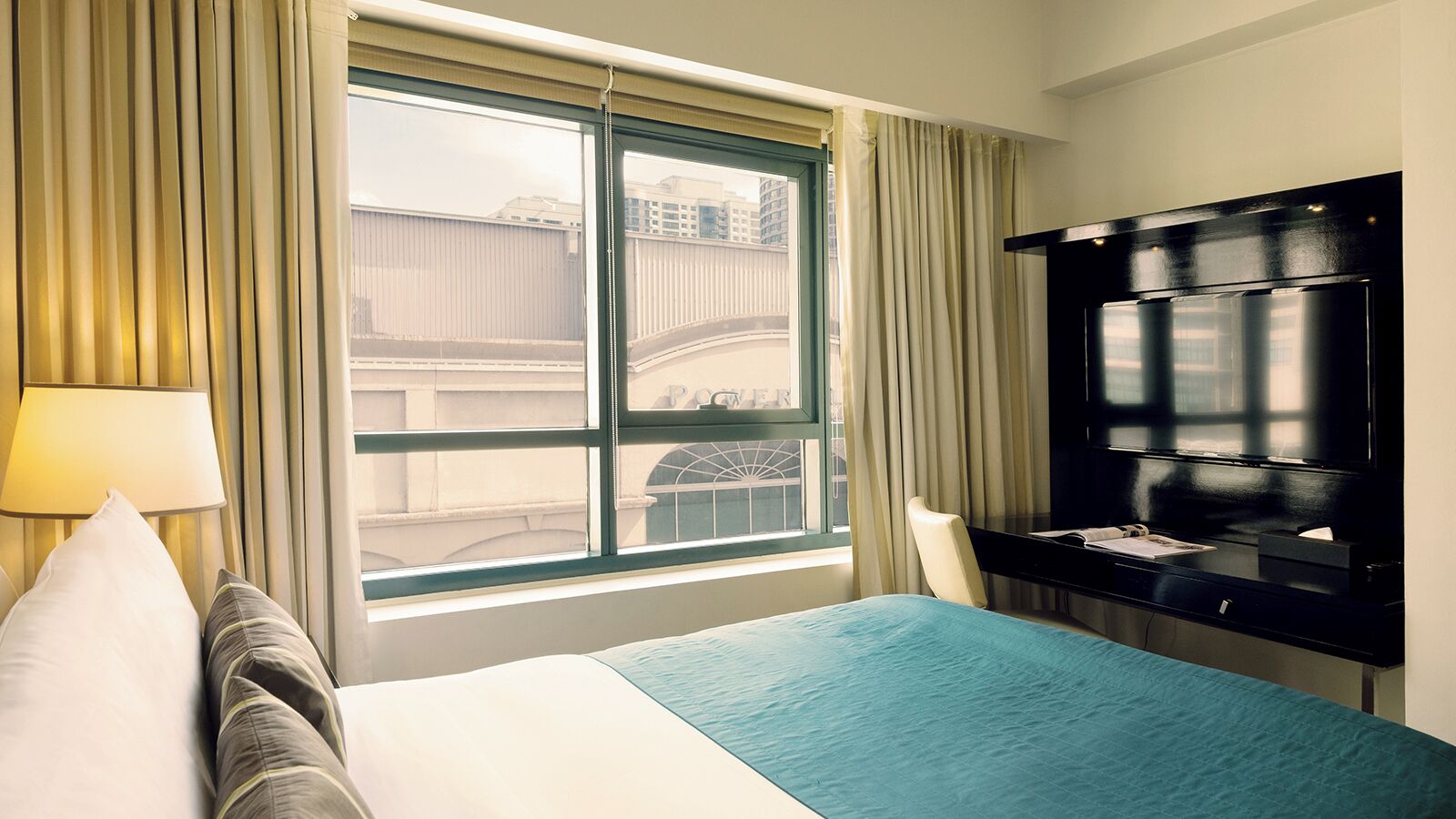 A hotel room with a bed, a desk, a chair, a TV, and a window with curtains.