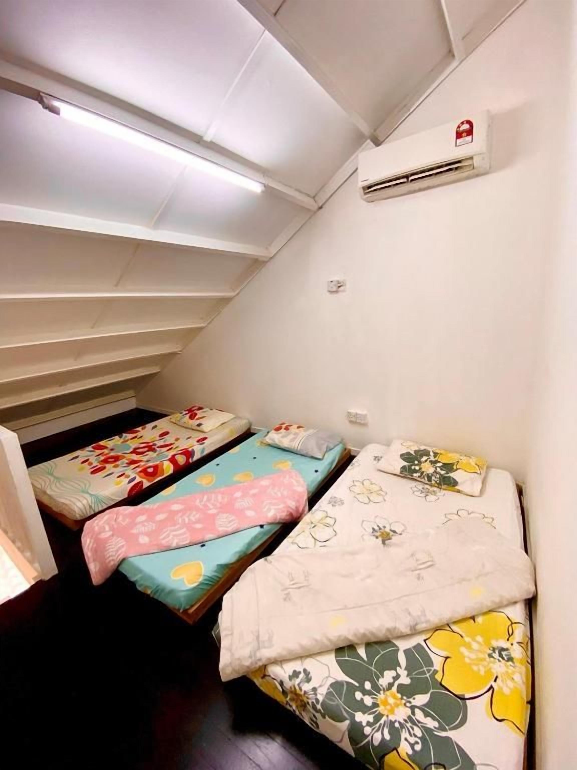 A room with three beds, each with different patterned bedding, a ceiling fan, and an air conditioning unit.