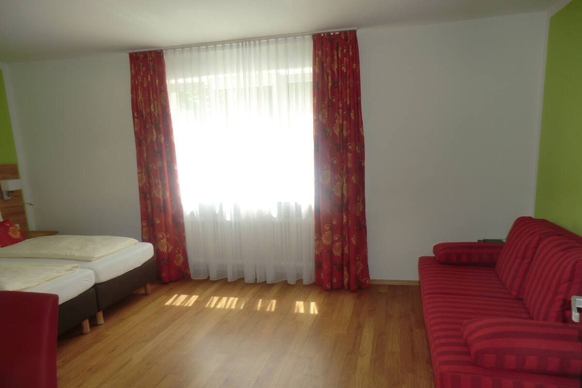 A room with a bed, a red sofa, and a window with curtains.