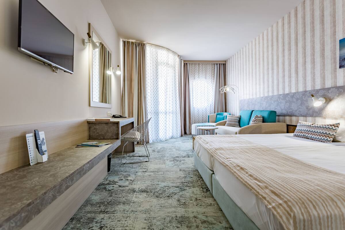 A hotel room with a bed, a desk, a TV, a chair, and curtains.