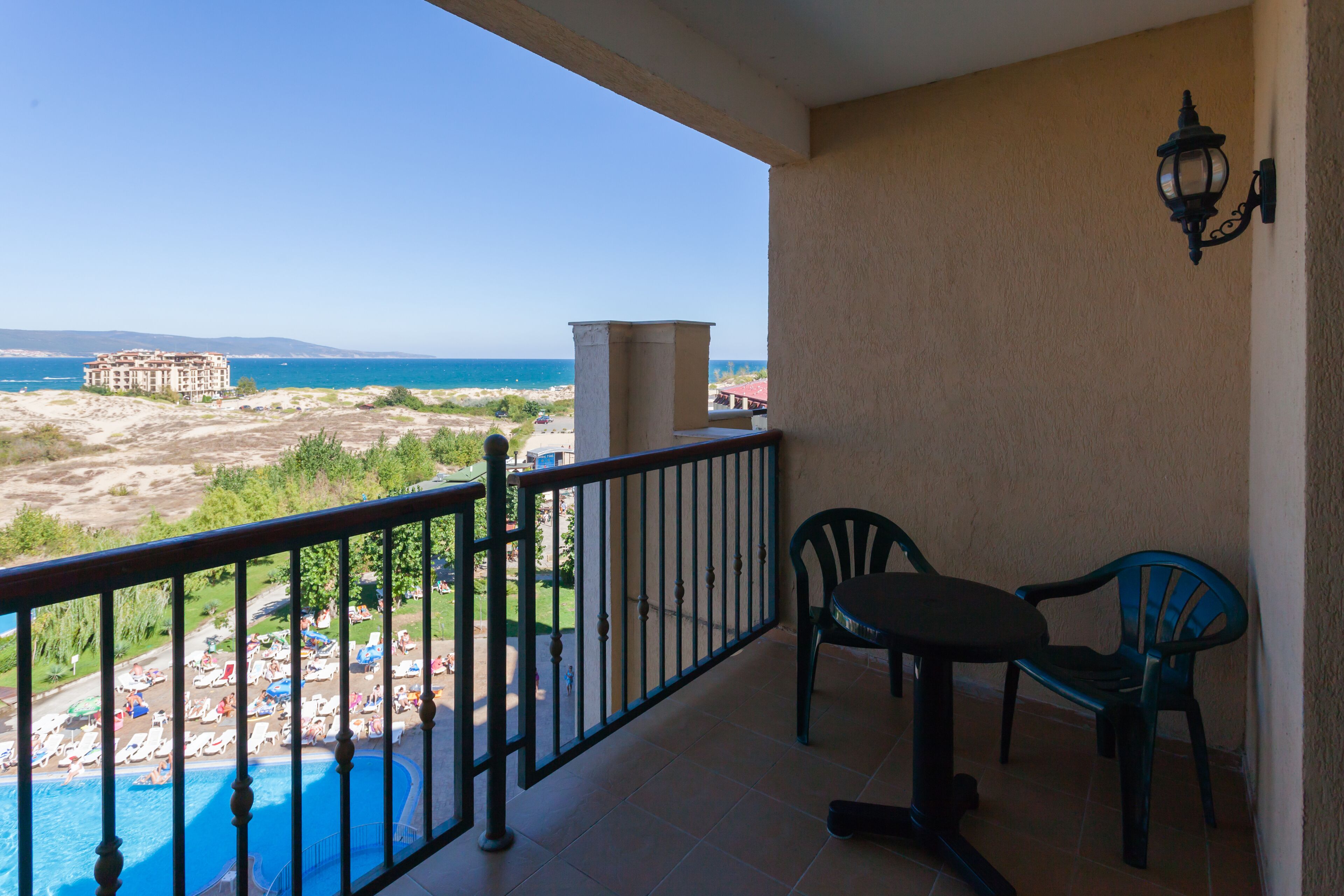 Uma varanda com vista para uma praia, uma piscina e um edifício ao longe.