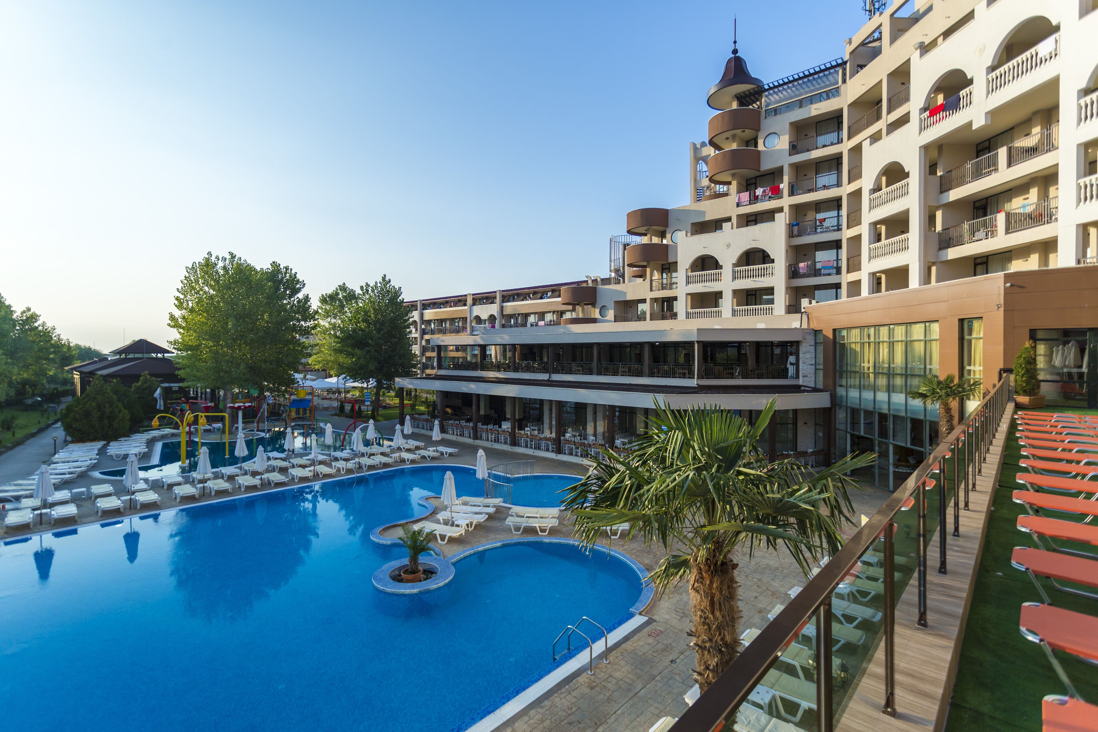 A hotel with a large swimming pool, multiple balconies, and outdoor seating areas.