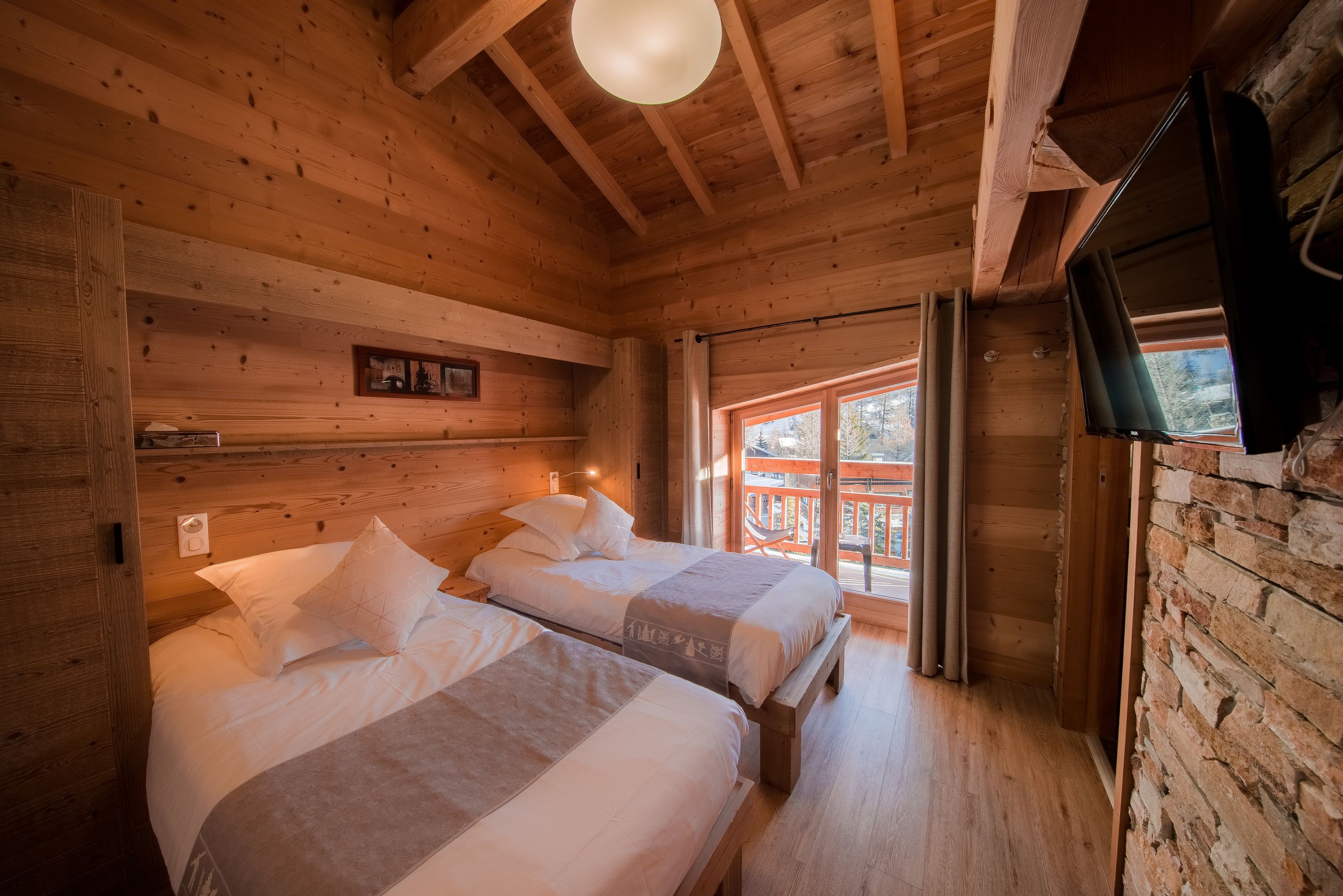 Une cabane en bois avec deux lits, une télévision et un balcon offrant une vue sur les arbres.