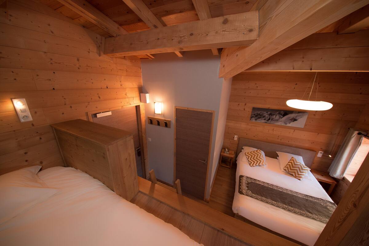 A wooden cabin room with two beds, a small table, and a door leading to another room.