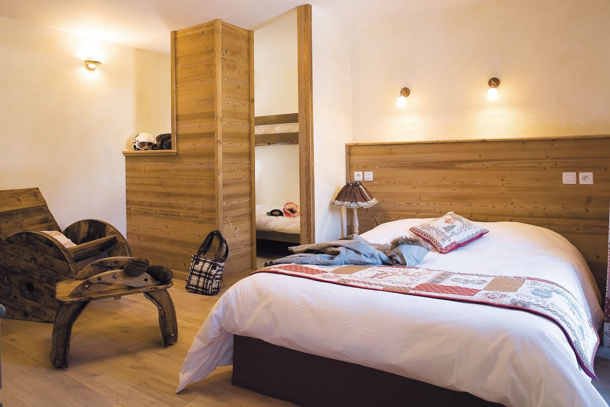 A bedroom with a wooden headboard, a bed with a quilt, a small wooden table, and a chair.