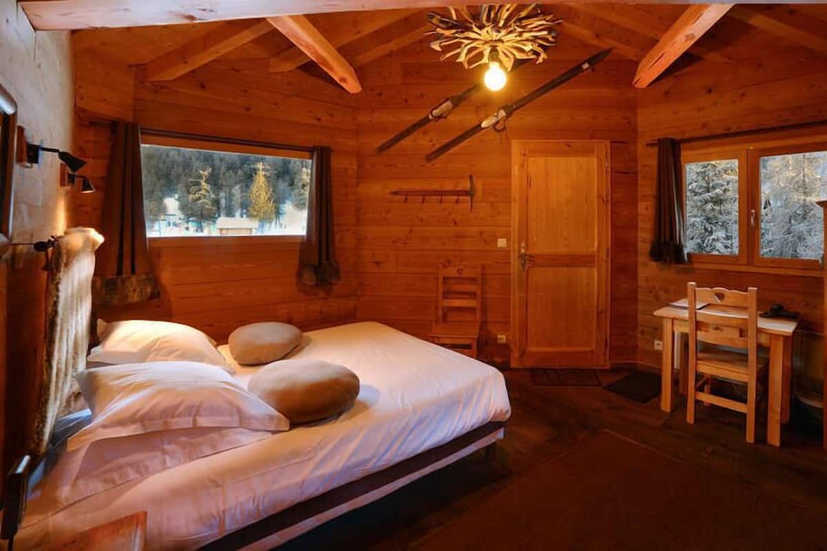 A cozy wooden cabin room with a bed, a desk, and a television.
