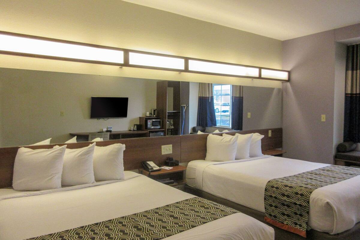A hotel room with two beds, a TV, a desk with a phone, and a window with curtains.