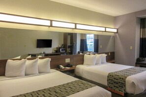 Two single beds with white linens and patterned bedspreads, a flat-screen TV, desk, and mirror.
